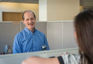 Two People Talking Across A Cubicle Wall