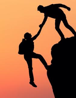 A Person helping Another Person Up a Mountain